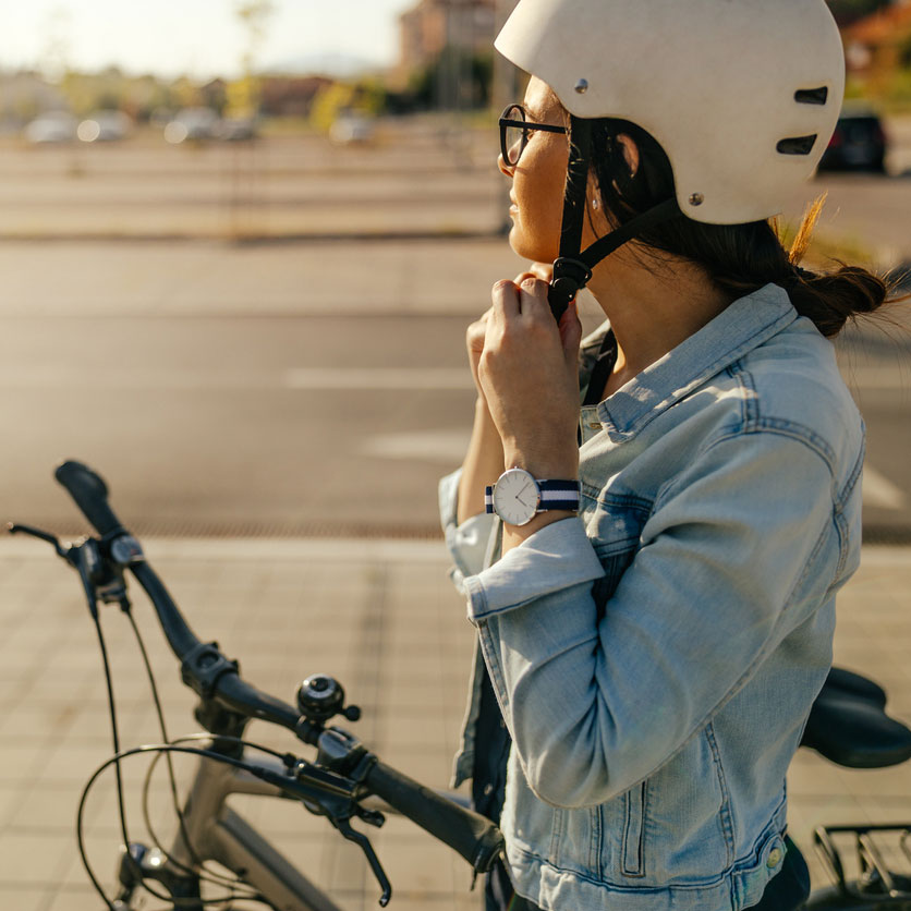 Kvinna vid cykel knäpper på sig cykelhjälm.