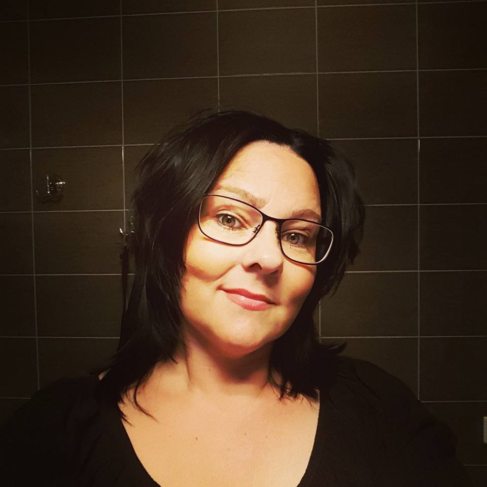 En kvinna med mörkt hår och mörk tröja tittar in i kameran och ler.