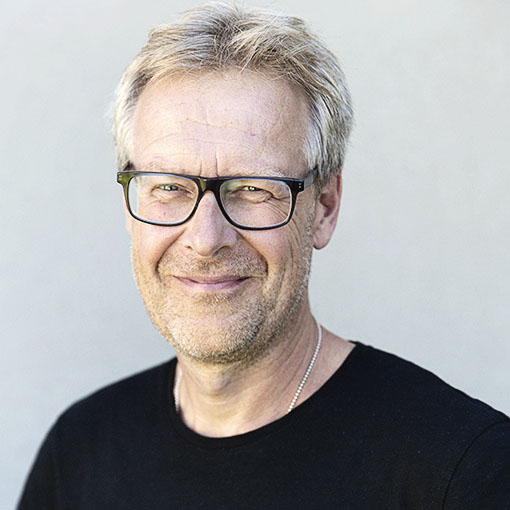 En man med blont hår och glasögon ler mot kameran.