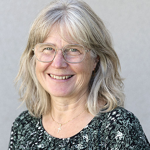 En kvinna med blont hår och mönstrad blus ler mot kameran.